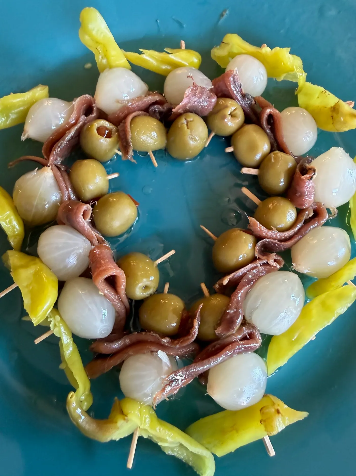 Skewers of olives, anchovies, pickled onions and guindilla peppers arranged in a ring on a blue plate