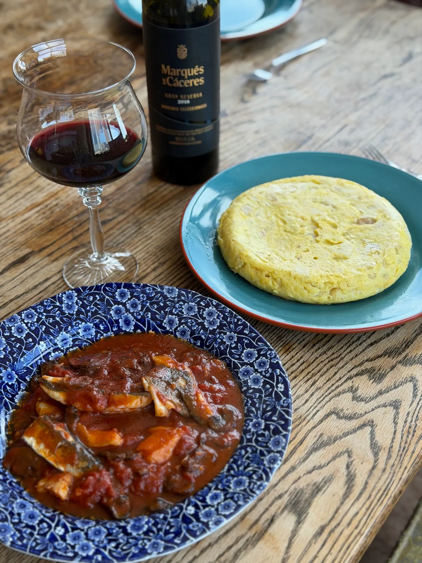 A table with red wine, a potato tortilla and a stew in a blue-and-white bowl