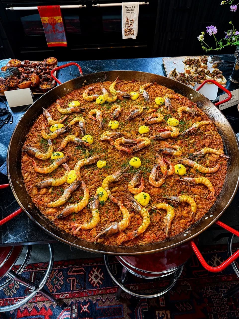 A wide paella pan of saffron rice topped with prawns, over a flame