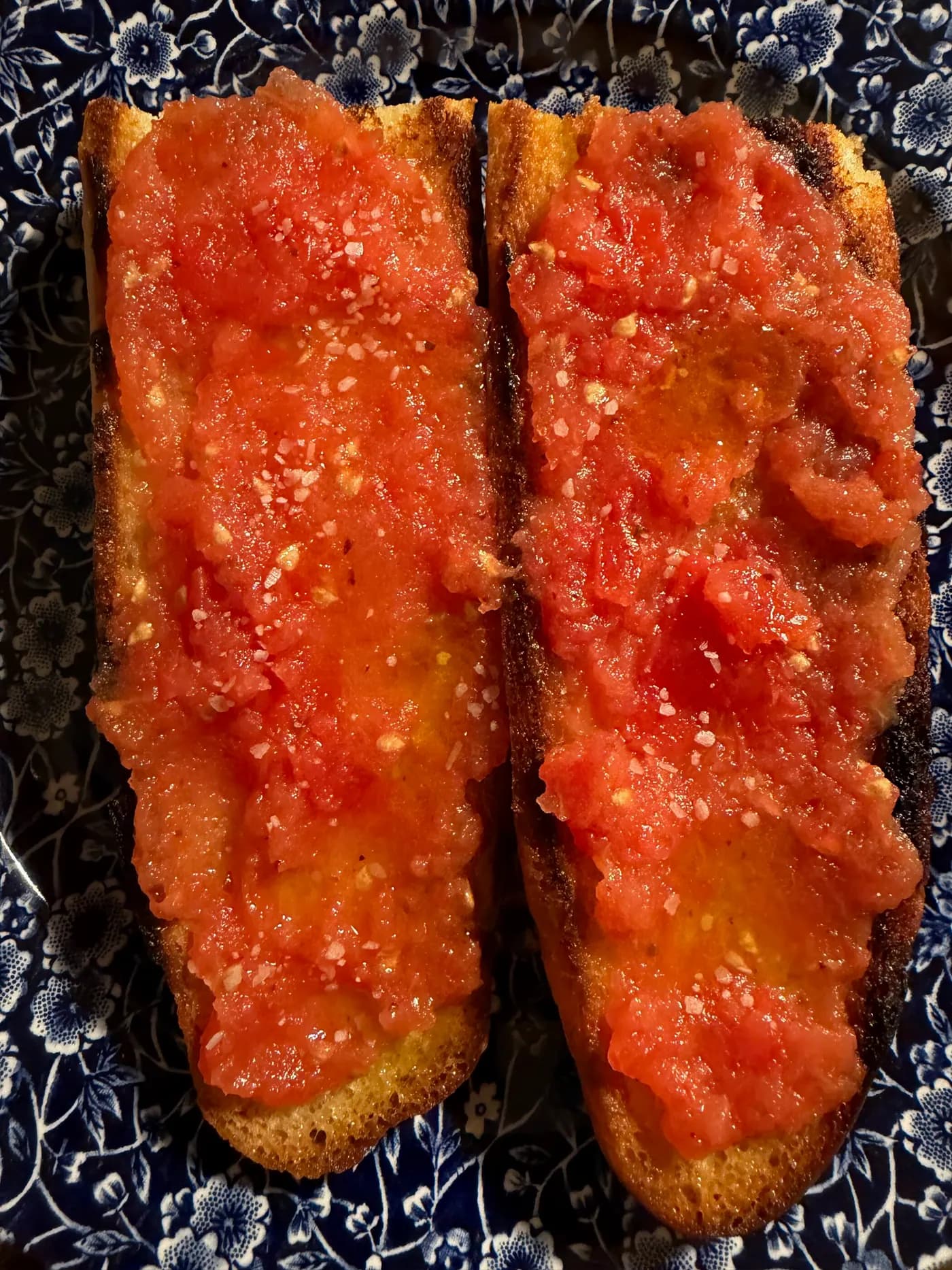 Two slices of toasted bread spread with grated tomato on a blue-and-white plate